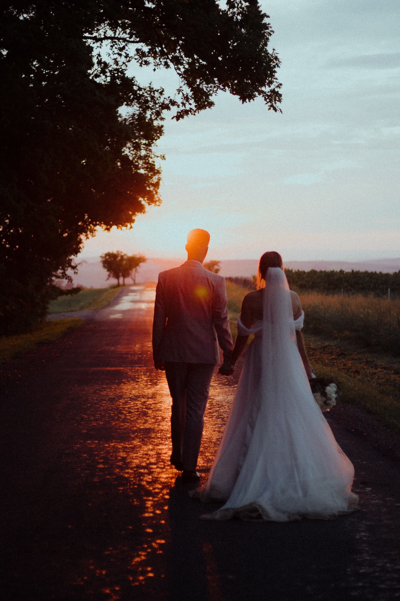 Newlyweds walking along a wet country road into the setting sun