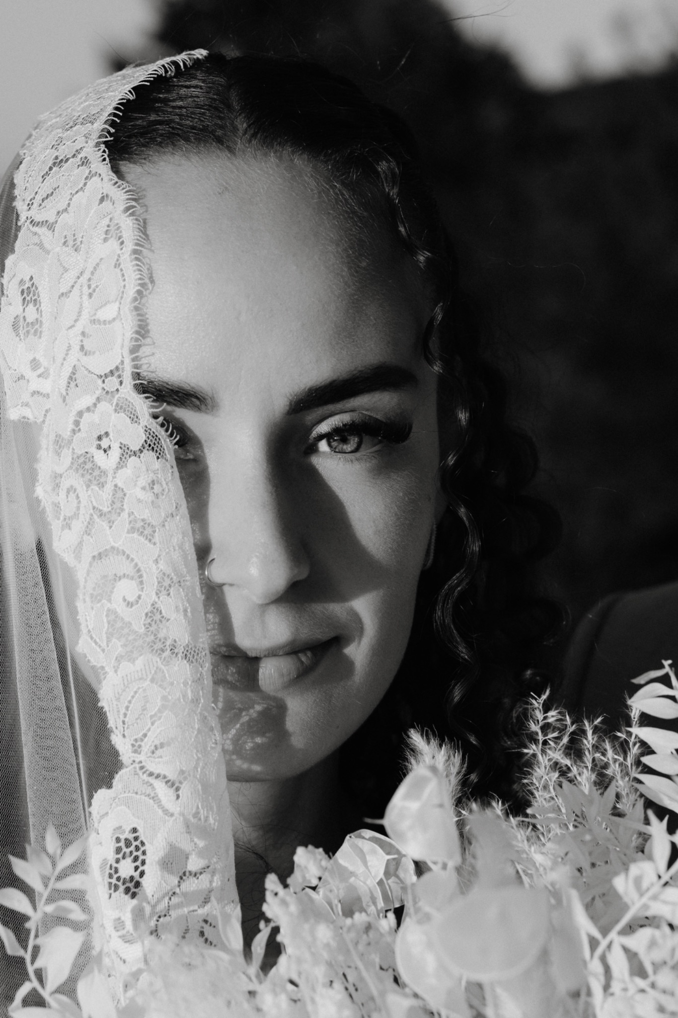 Black-and-white bridal portrait with a lace veil covering part of her face